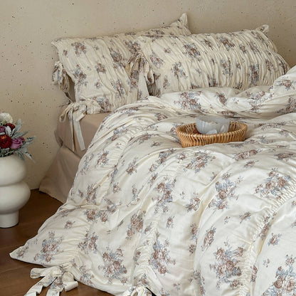 Cream floral cotton muslin bedding set with matching ruched pillow shams, ribbon ties, and warm vintage cottage styling.