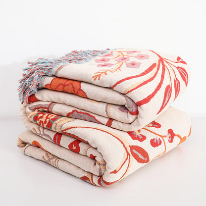 The jacquard cotton throw blanket folded neatly in a stack of two, revealing the large-scale floral design in red, orange, and beige. The multi-colored fringe is visible on the top edge of the stack.