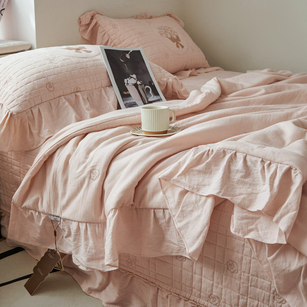 Close-up of the pink quilted bedding texture, showing the detailed rose bouquet embroidery and a folded ruffled edge.