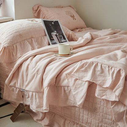 Close-up of the pink quilted bedding texture, showing the detailed rose bouquet embroidery and a folded ruffled edge.
