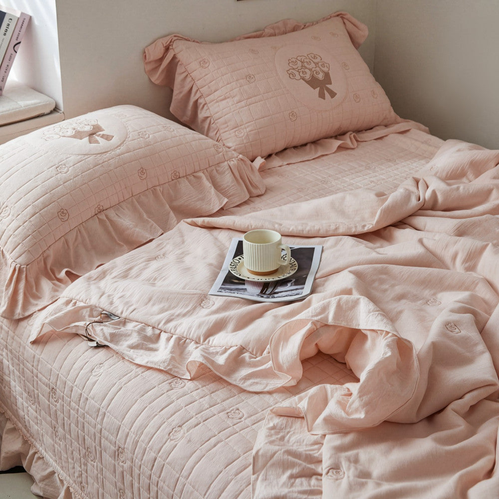 High-angle view of the pink quilted bedding set, highlighting the diamond-stitch pattern, rose embroidery, and a ruffled bedskirt.