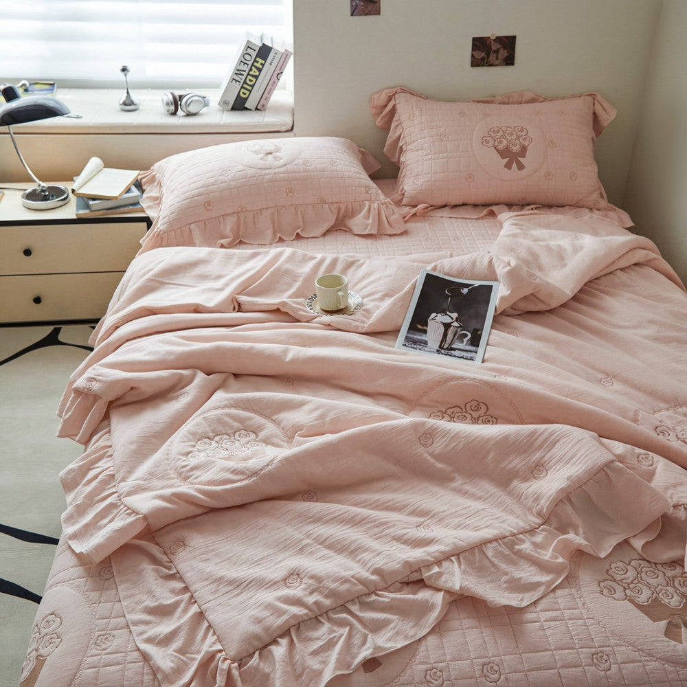 French embroidered style bedding set in pink, featuring ruffled pillowcases with bow accents and a matching quilted coverlet.