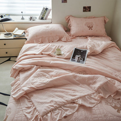 French embroidered style bedding set in pink, featuring ruffled pillowcases with bow accents and a matching quilted coverlet.