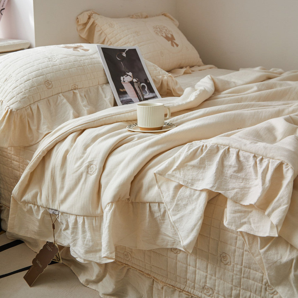 Close-up of the cream quilted bedding texture, showing the central rose bouquet embroidery and delicate ruffled edges.