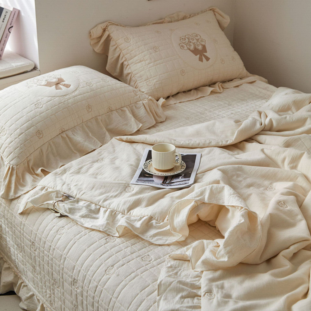 High-angle view of the cream quilted bedding set, highlighting the subtle diamond-stitch pattern and French embroidered rose accents.