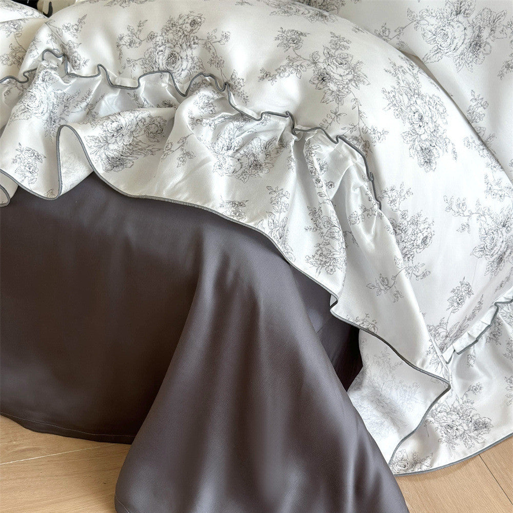 Close-up of French style Lyocell floral ruffle duvet cover with grey trim, draped over a solid grey bed sheet.