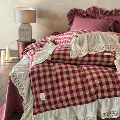 Bed with red and white checkered bedding and lace details, next to a lamp and candles on a wooden floor.