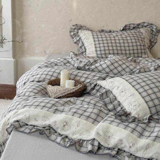 Grey plaid cotton muslin bedding set with ruffled trim and embroidered animal designs on a bed