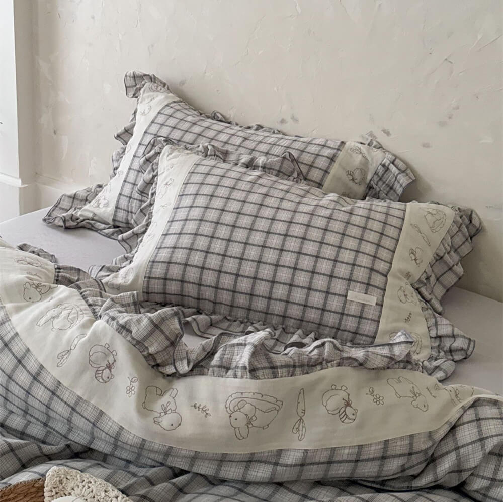Grey plaid cotton muslin bedding set with ruffled trim and animal embroidery on a bed
