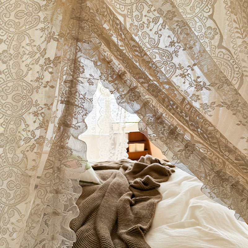 Lace bed canopy curtains with floral pattern over cozy bedding and soft knit blanket