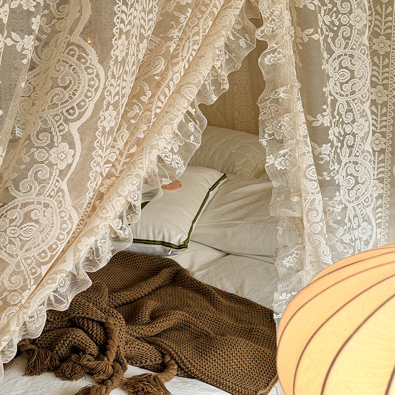 Lace bed canopy curtains on four-poster bed with cozy white pillows and brown knit blanket