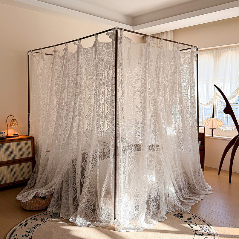 Sheer white lace canopy curtains draped over a four-poster bed in a cozy sunlit bedroom.