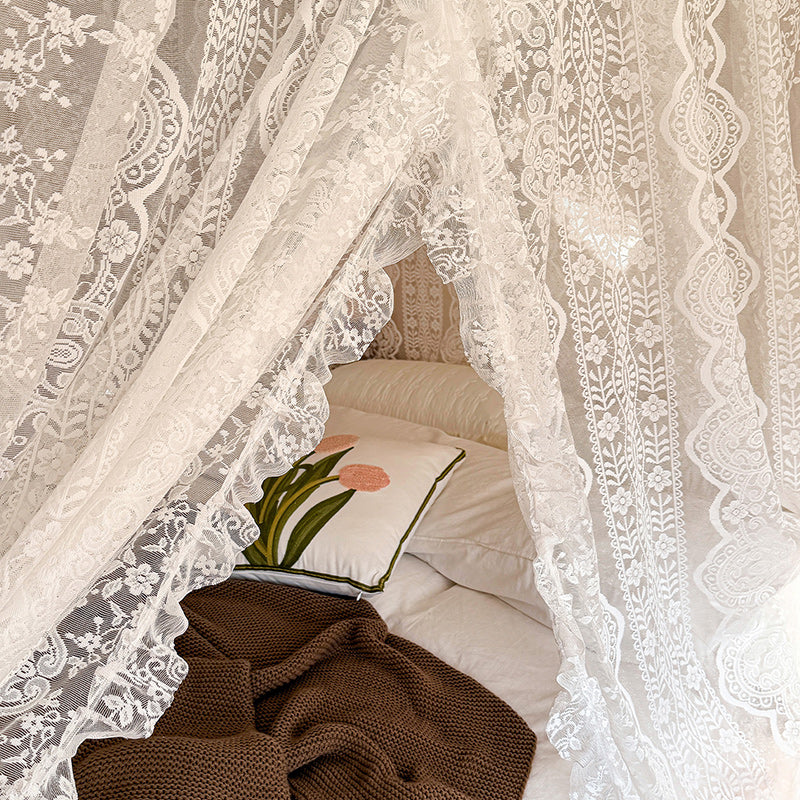 Lace bed canopy curtains with floral pattern over cozy bedding and a decorative pillow.
