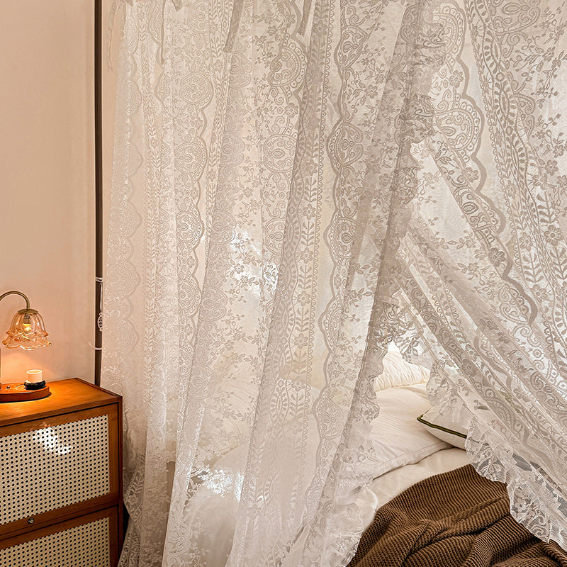 Lace bed canopy curtains on a 4-poster bed with cozy bedding in a warm bedroom setting