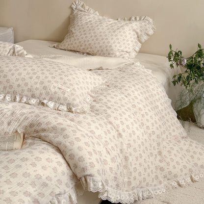 Close-up of a vintage floral duvet cover and matching ruffled pillowcases in muted pink rose patterns with delicate eyelet lace trim detailing.