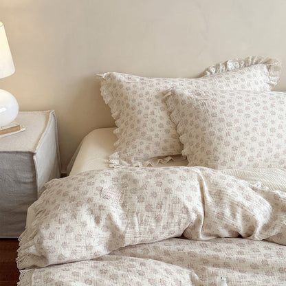 Soft focus view of an aesthetic layered bed with dusty pink rosebud prints, ruffled duvet cover, and warm, inviting bedroom lighting.