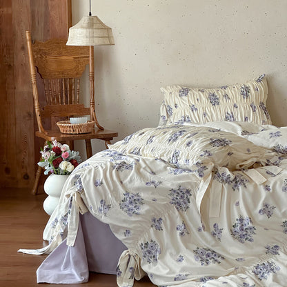 Lavender floral cotton muslin bedding set with ruched pillows, ribbon-tie duvet details, and soft cottage bedroom styling.