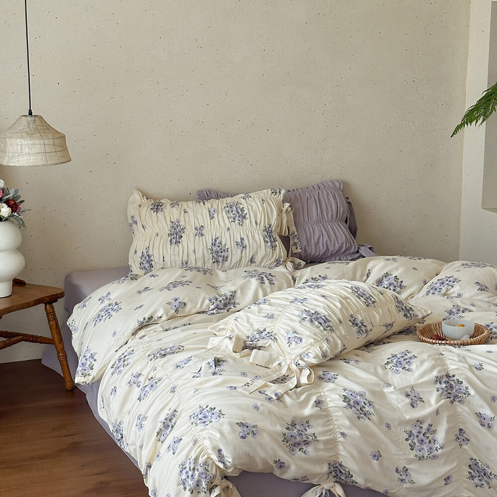 Cream cotton muslin bedding set with lavender floral print, gathered ruching, matching pillow shams, and lavender sheet.