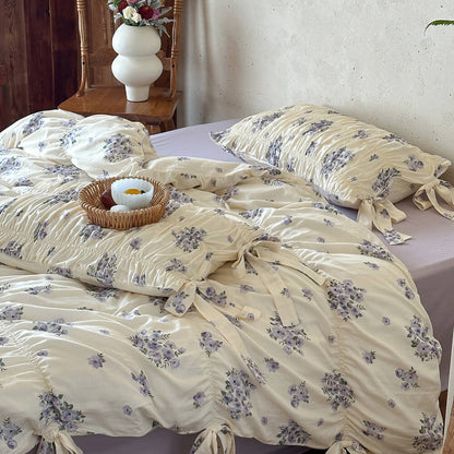 Lavender floral bedding set styled in a warm cottage bedroom with ribbon ties, ruched texture, and wooden decor accents.