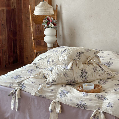 Lavender floral bedding with ribbon-tie details, ruched duvet surface, and cream cotton muslin fabric on a lavender sheet.