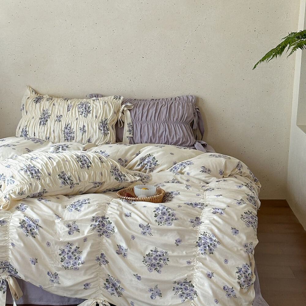Full view of lavender floral cotton muslin bedding styled with ruched pillows, lavender sheet, and calm neutral bedroom decor.