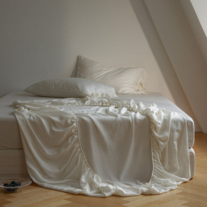 A bed dressed in white bedding, including a white sheet with ruffled edges and two white pillows, set in a softly lit attic bedroom with light wood flooring.