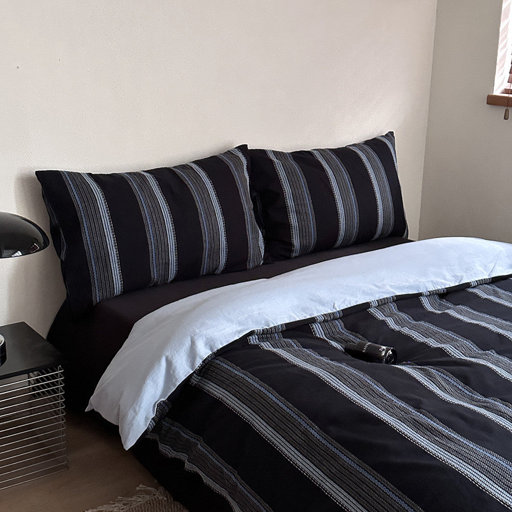 Modern deep blue and gray striped jacquard cotton bedding set with pillowcases on bed