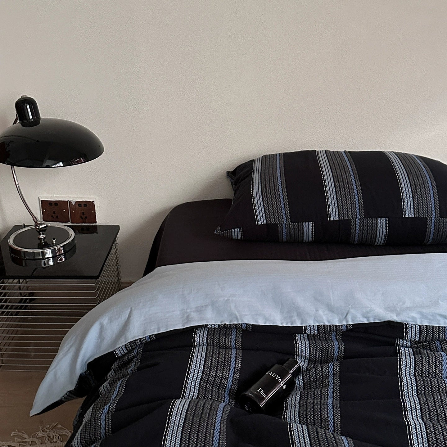 Modern deep blue jacquard cotton bedding set with striped pillow and comforter beside a black bedside lamp