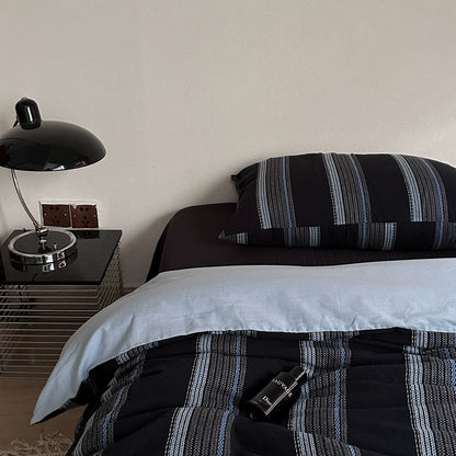 Modern deep blue jacquard cotton bedding set with striped pillow and comforter beside a black bedside lamp