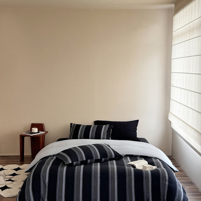 Modern bedroom with deep blue striped cotton bedding set, a wooden side table, and natural light