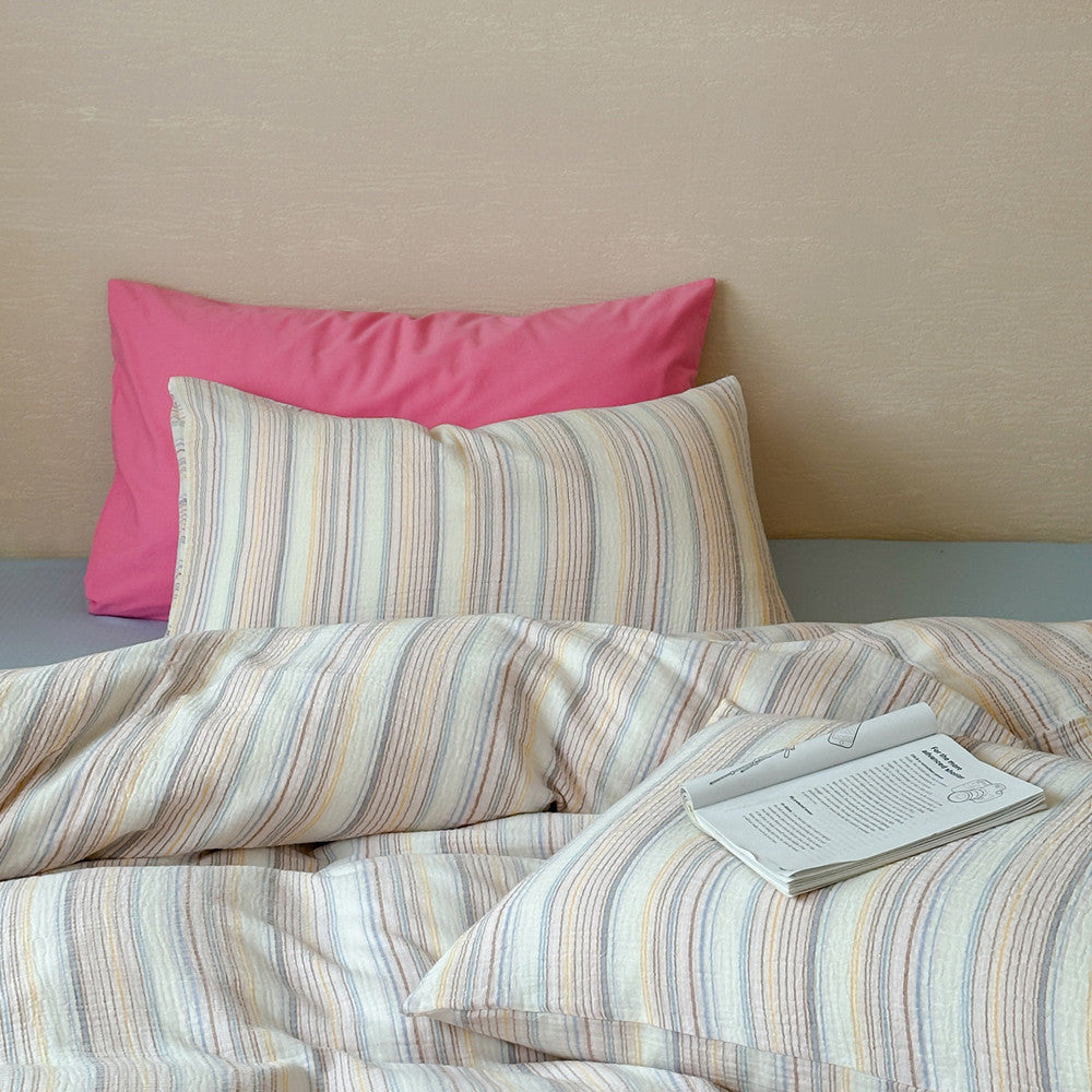 Modern striped duvet cover set with pastel lines, pink pillow, and open book on bed