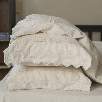 Stack of Natural Linen Cotton pillow shams with various lace and embroidered trim details, displaying the off-white color and the light, relaxed feel of the bedding set.