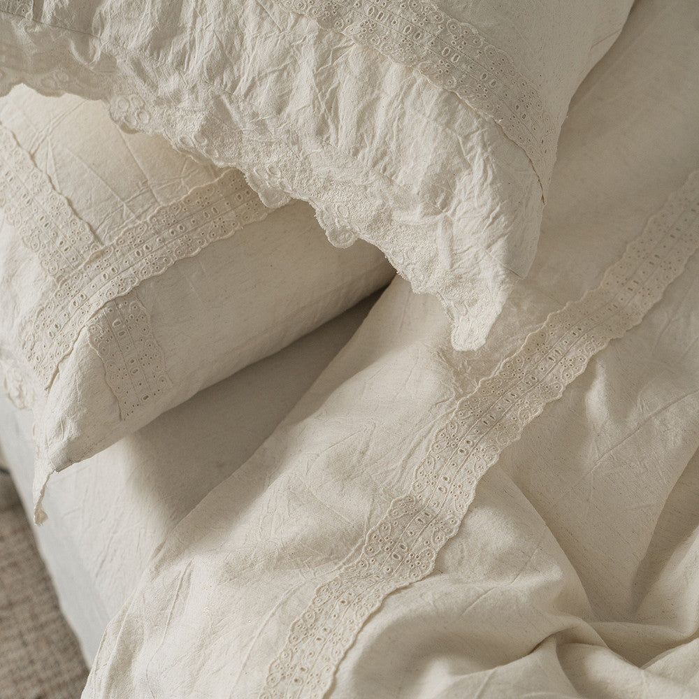 Close-up overhead view of the Natural Linen Cotton fabric and lace detailing on a pillow sham and the duvet cover, focusing on the wrinkled texture and the elegant crochet/eyelet trim.