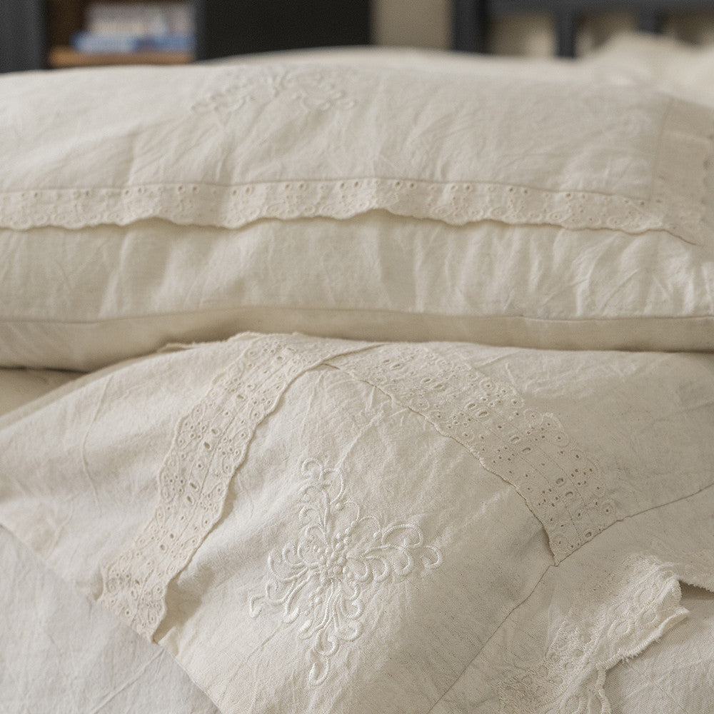 Close-up showing the layered textures of the Linen Cotton Bedding Set, including a pillowcase with a simple lace band and a throw pillow with a central embroidered floral design.