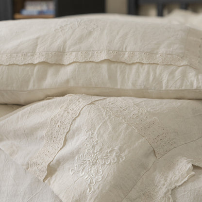 Close-up showing the layered textures of the Linen Cotton Bedding Set, including a pillowcase with a simple lace band and a throw pillow with a central embroidered floral design.