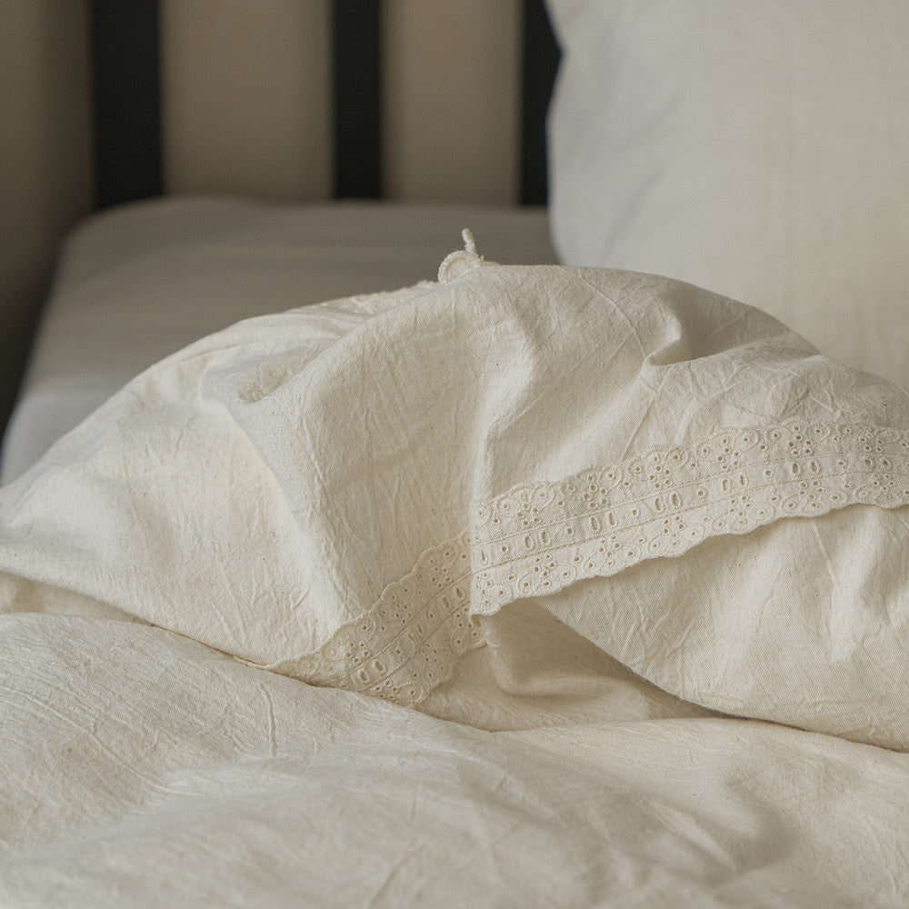 A draped section of the Natural Linen Cotton Duvet Cover on a bed, focusing on the soft folds and the elegant eyelet lace insert along the edge of the fabric.