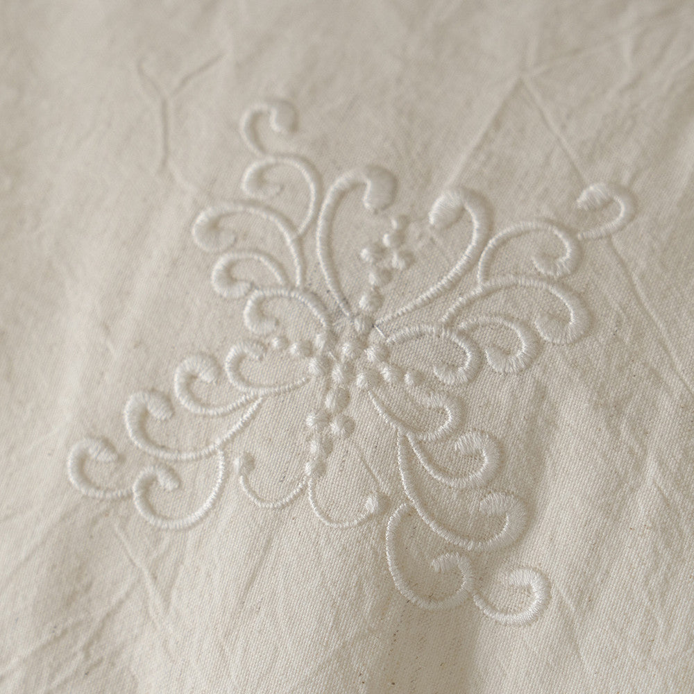 Macro close-up of the delicate white embroidered floral pattern featured on the Natural Linen Cotton Bedding Set, showcasing the stitch work detail.