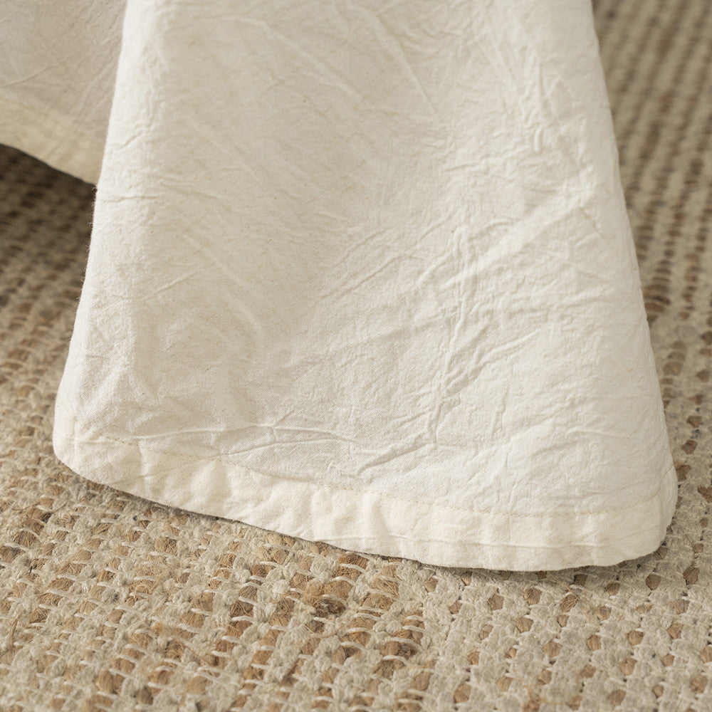 Close-up of the simple hem and crinkled texture of the Natural Linen Cotton fabric, placed on a woven jute or sisal rug, emphasizing the rustic and organic feel.