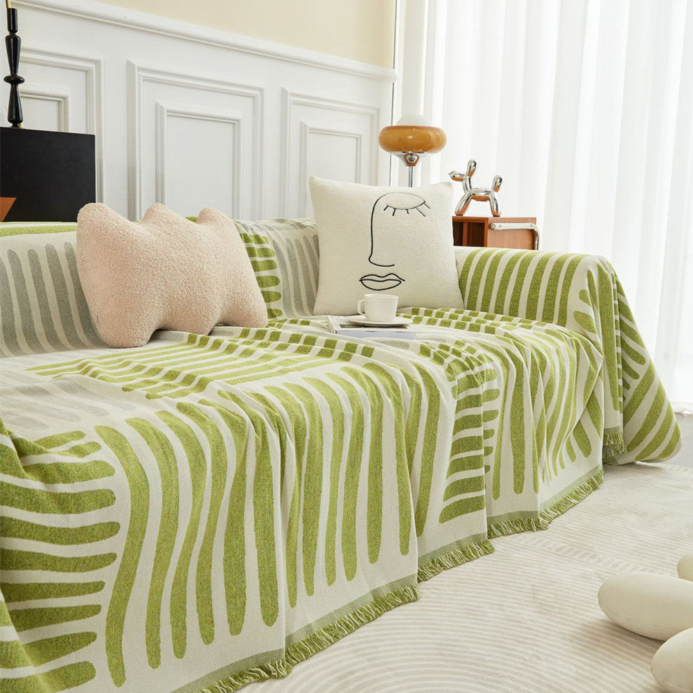 Green geometric one-piece reversible sofa cover with abstract pillows in a bright modern living room