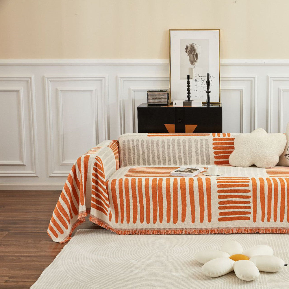 Modern living room with orange and beige geometric reversible sofa cover, plush pillows, and framed art