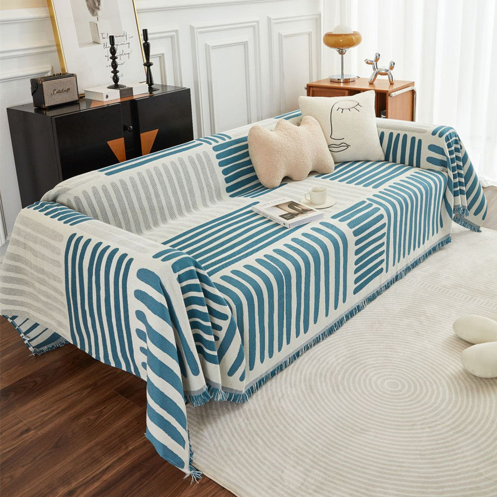 Modern living room with a blue and white geometric reversible sofa cover, decorative pillows, and cozy cotton decor.