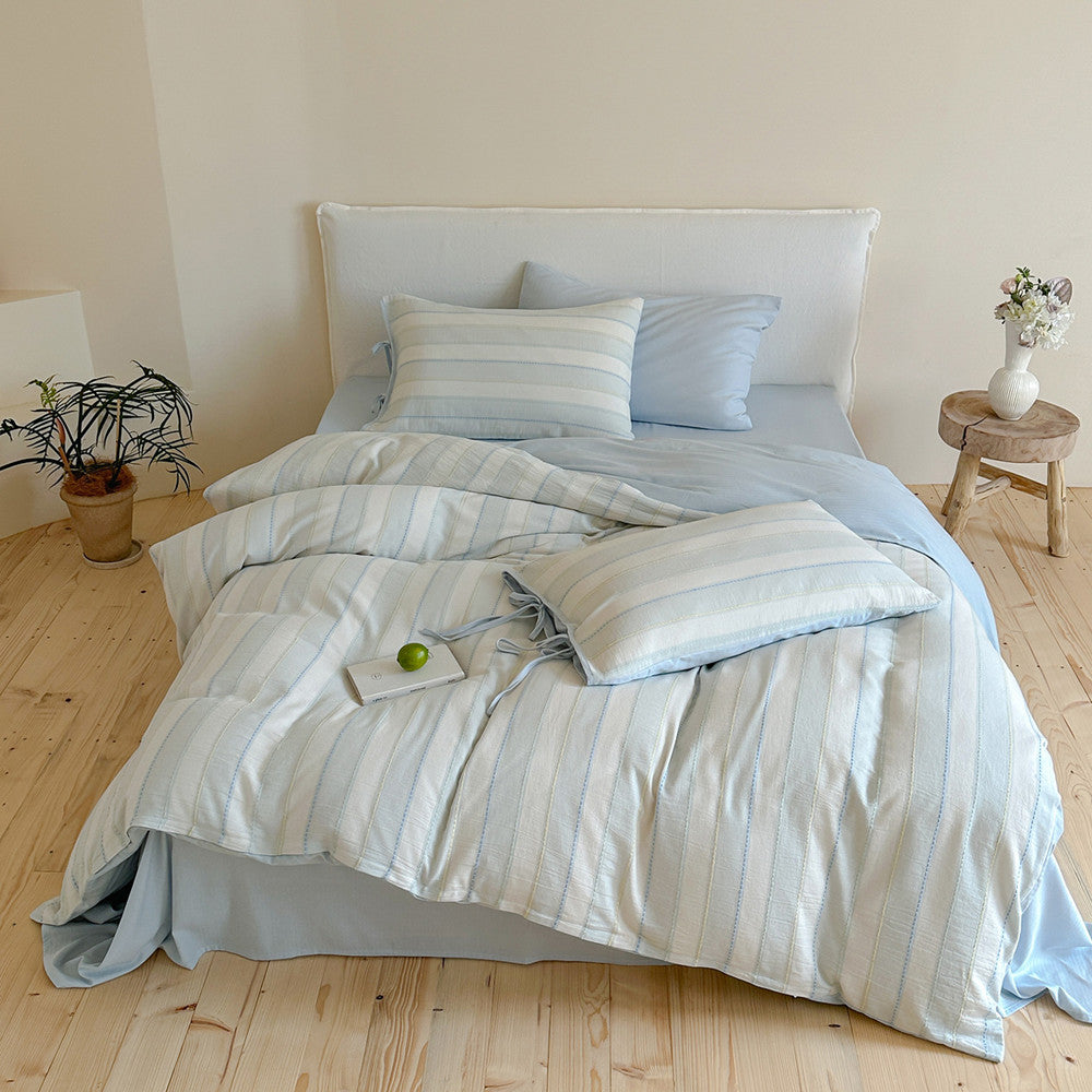 Full view of the blue Pastel Cotton Striped Bedding Set styled in a cozy, light-filled bedroom with wood floor.
