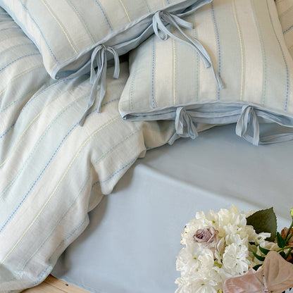 Close-up detail of the blue cotton striped pillow with decorative ribbon ties and matching solid color sheet.