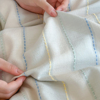 Hands touching the blue cotton striped fabric, emphasizing the soft, lightweight, woven texture of the bedding.