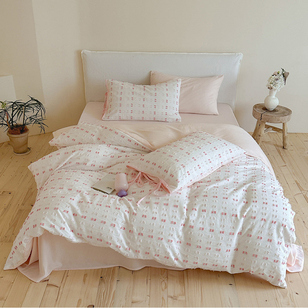 Full view of the Pastel Pink Tufted Check Cotton Bedding Set on a bed, showcasing the tufted squares duvet cover, pink solid sheets, and coordinating pillow shams with ribbon ties, styled in a minimalist bedroom