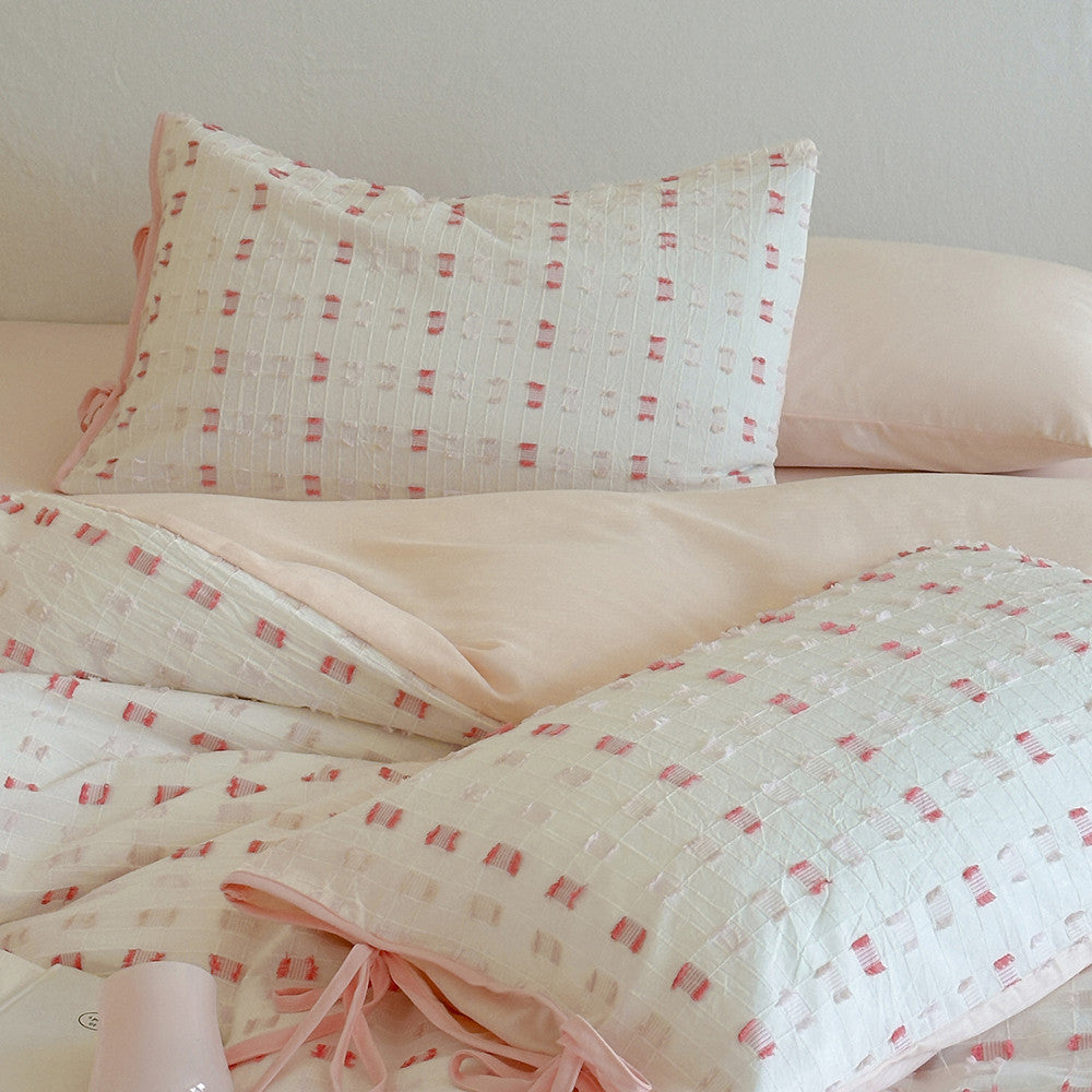 Close-up showing the layered Pastel Pink Tufted Check Pillow Shams and the smooth solid pink fitted sheet/duvet cover, with a focus on the decorative ribbon ties on the pillow closures.