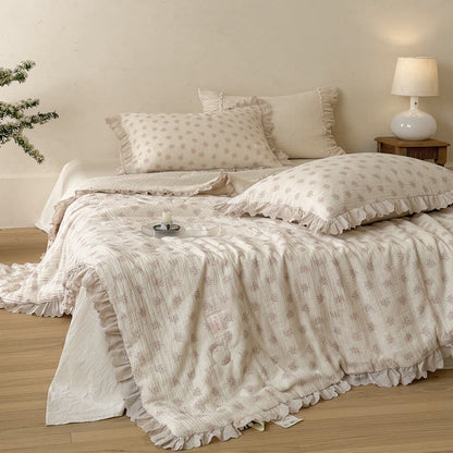 Pink floral cotton comforter with ivory ruffled lace trim styled on a soft cottage bed