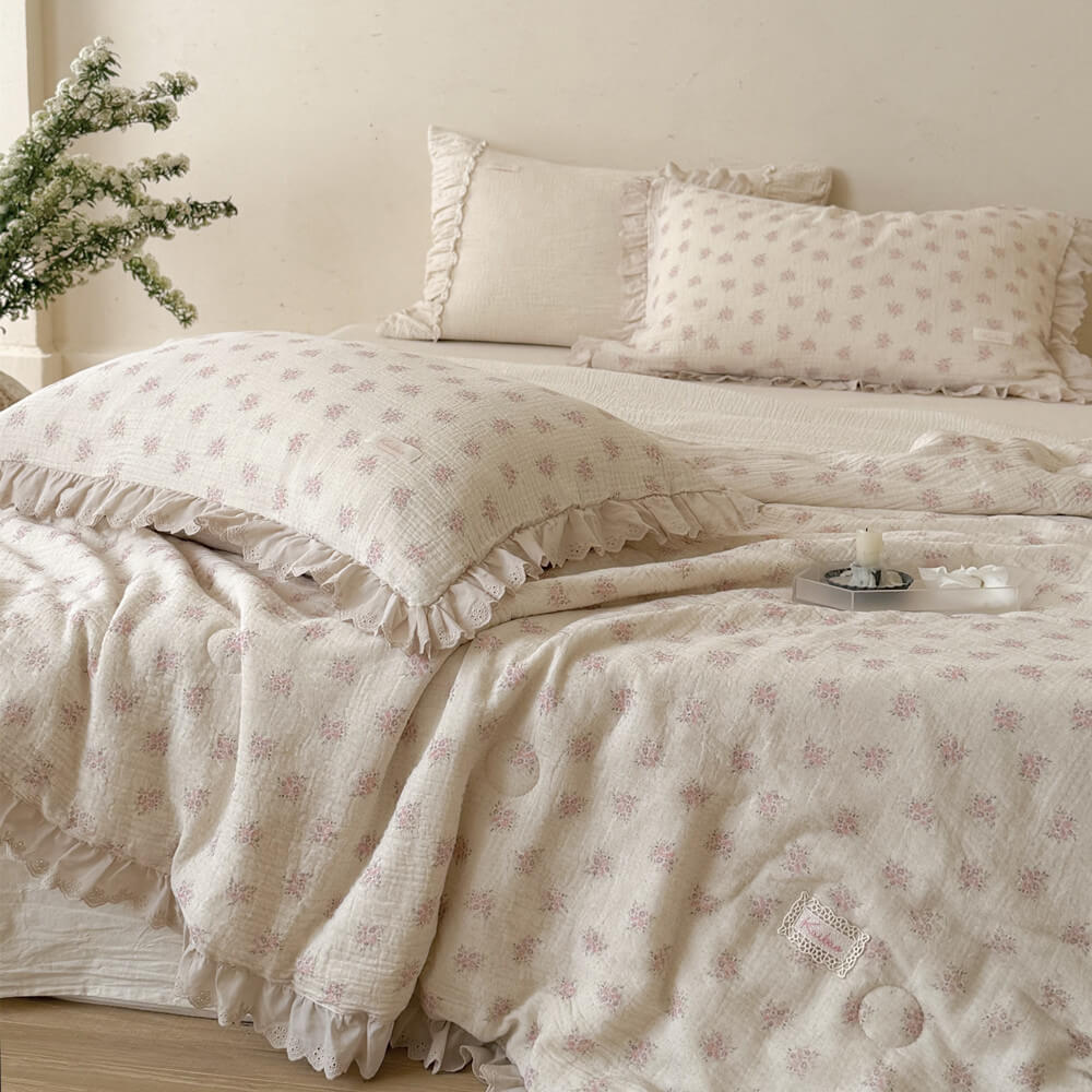 Pink floral comforter draped across an ivory bed with matching styled pillows