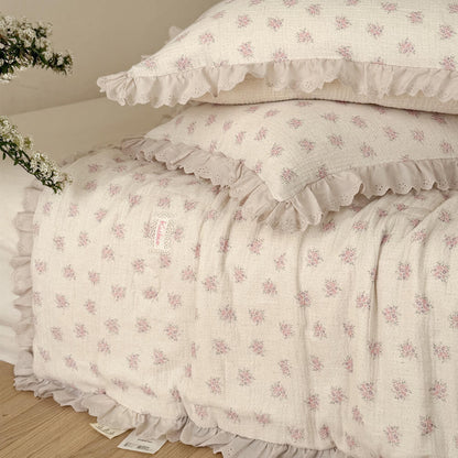Close view of pink floral cotton comforter showing ivory ruffled lace trim and crinkled texture