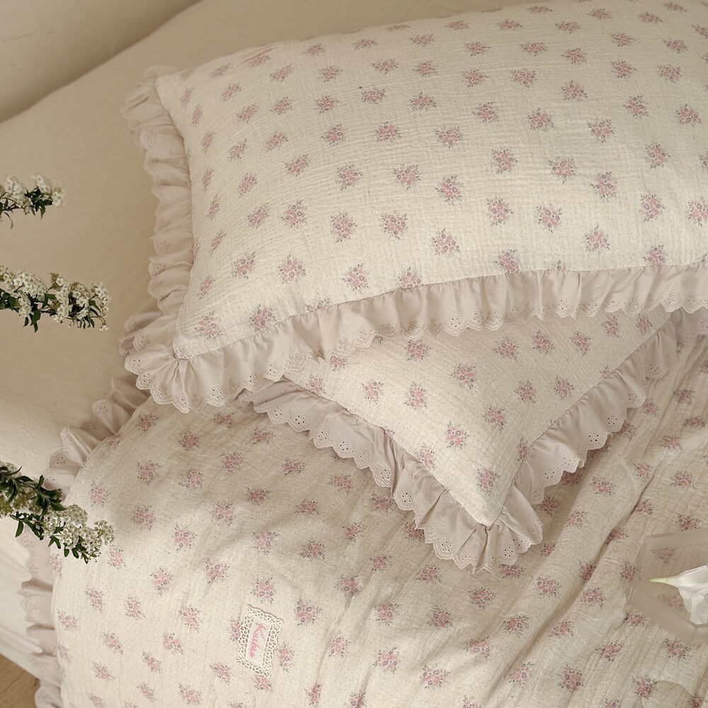 Matching pink floral pillows and comforter with ivory ruffled lace trim on a neutral bed